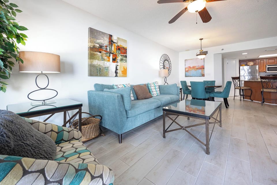 Bright living area features a turquoise sofa, patterned chairs, and a dining set, creating a welcoming vibe for relaxation