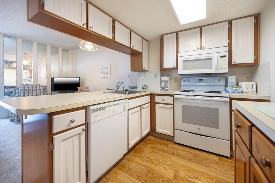The kitchen features white cabinetry, essential appliances, and a view into the living area with a TV, perfect for gatherings