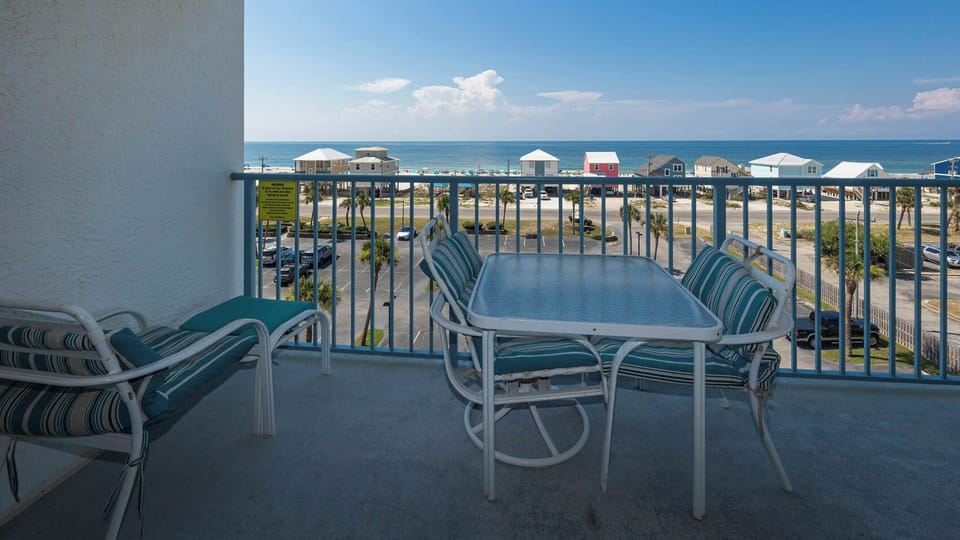 Enjoy a relaxing view from the balcony with teal-striped seating overlooking the beach and vibrant coastal homes