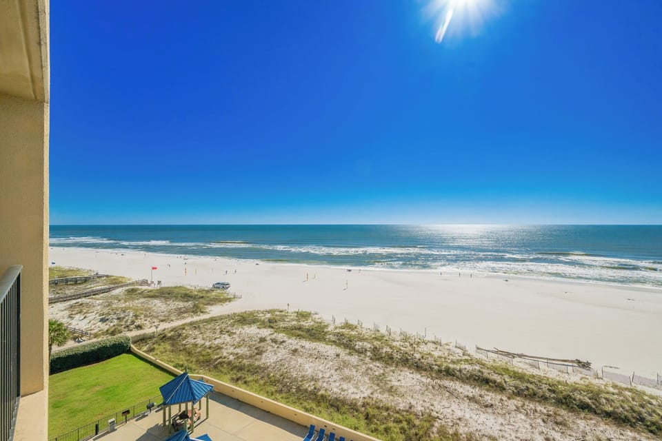 A clear view showcases the expansive beach with soft white sand and gentle waves under a bright blue sky
