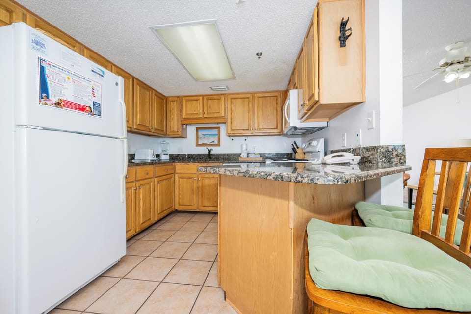 The fully-equipped kitchen features warm wooden cabinetry, a stylish countertop, and a breakfast bar with cushioned seating