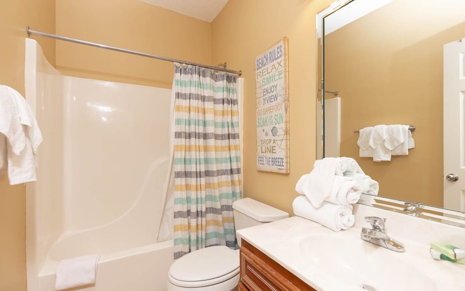 Striped shower curtain complements the warm tones of the guest bathroom, featuring a spacious vanity and fresh towels