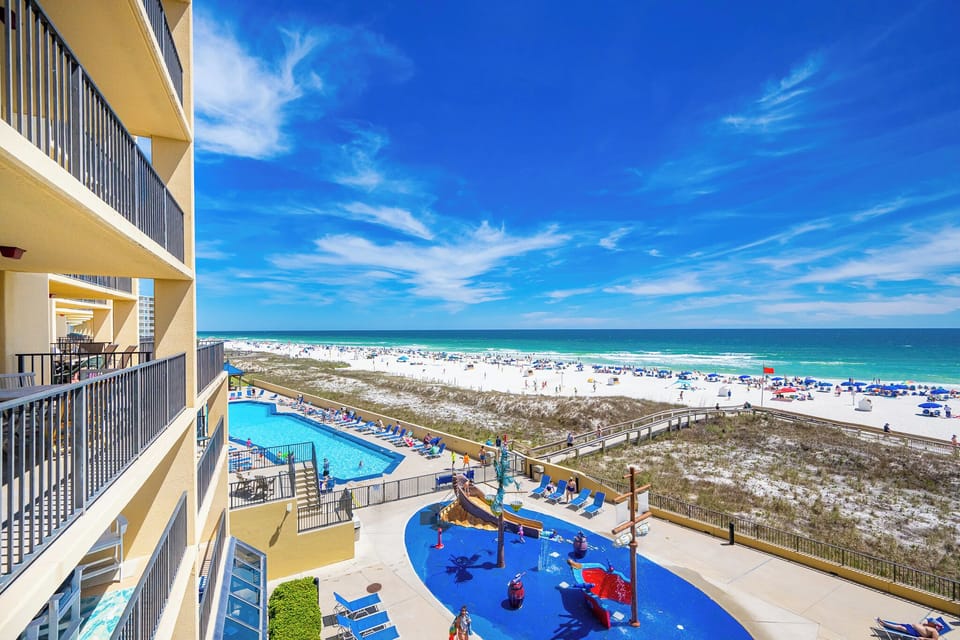 A lively pool sparkles below while you admire beachside fun and clouds drifting across deep blue sky