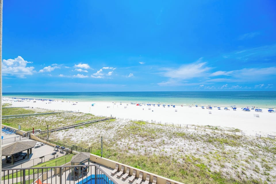 The vibrant beach front features white sand and colorful umbrellas under a clear blue sky, perfect for a relaxing getaway