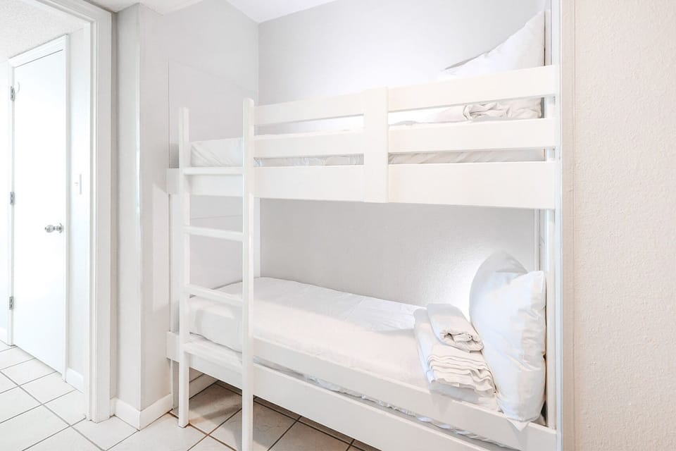 Sleep comfortably in the bright bunk space in the hall featuring a white bunk bed and fresh linens, perfect for kids