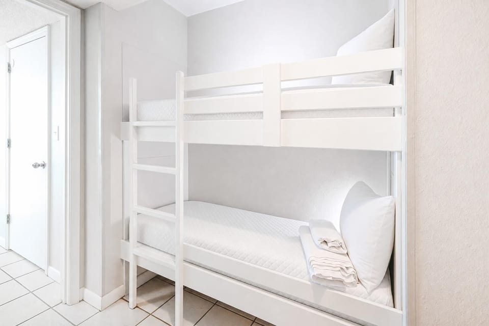 Sleep comfortably in the bright bunk space in the hall featuring a white bunk bed and fresh linens, perfect for kids