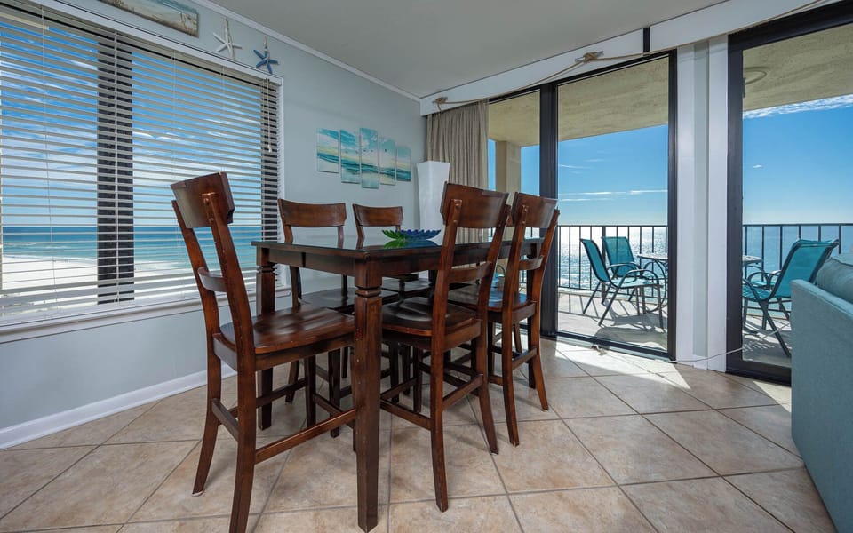 This dining area features a stylish wooden table with high-backed chairs and a beautiful view of the sparkling water beyond