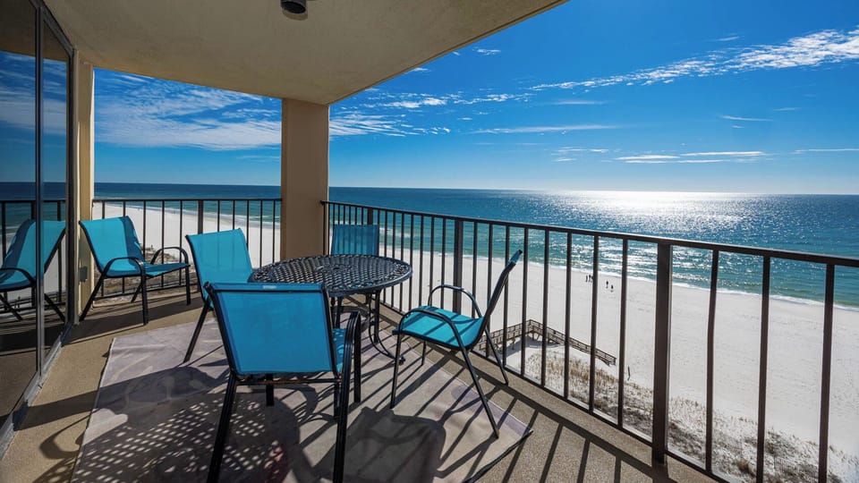 Relax on the balcony with turquoise chairs, a round table, and breathtaking views of the sandy shore and sparkling water
