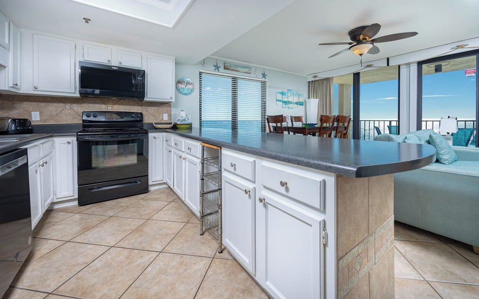 This kitchen features sleek black and stainless appliances, a spacious countertop, and a lovely view of the beach