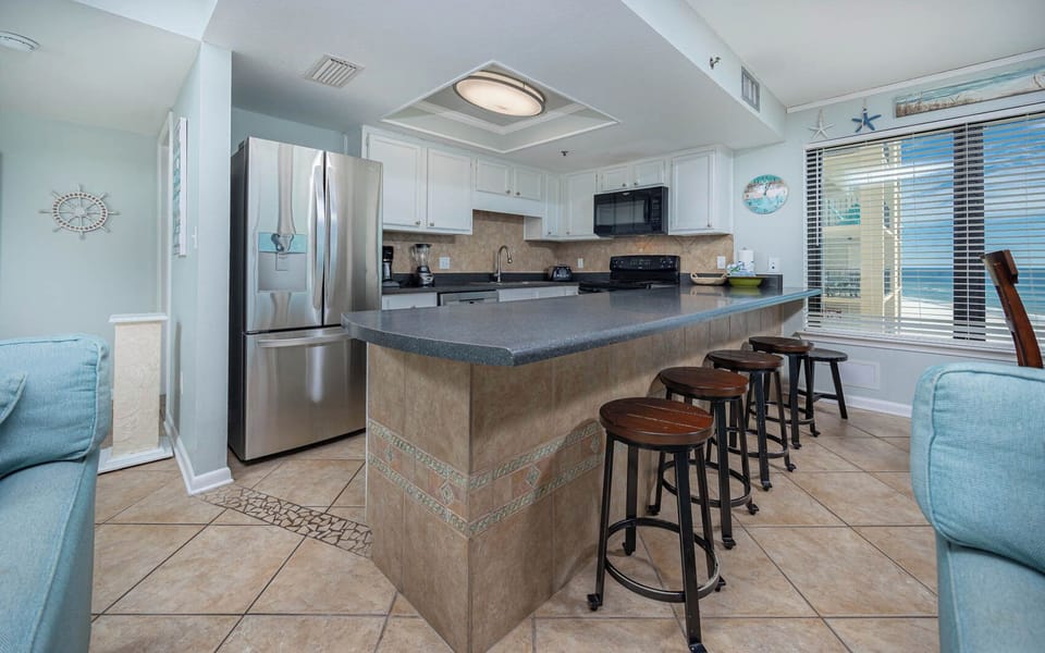 This modern kitchen features black and stainless appliances, a breakfast bar, and a beautiful view of the beach