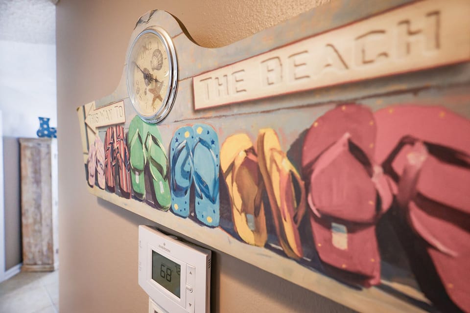 Discover a charming wall art piece featuring colorful flip-flops and a clock, adding a fun beach vibe to your stay