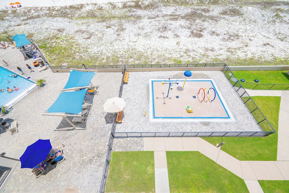 Relax at the outdoor splash park area, with a view of the beach and inviting lounge chairs under colorful umbrellas