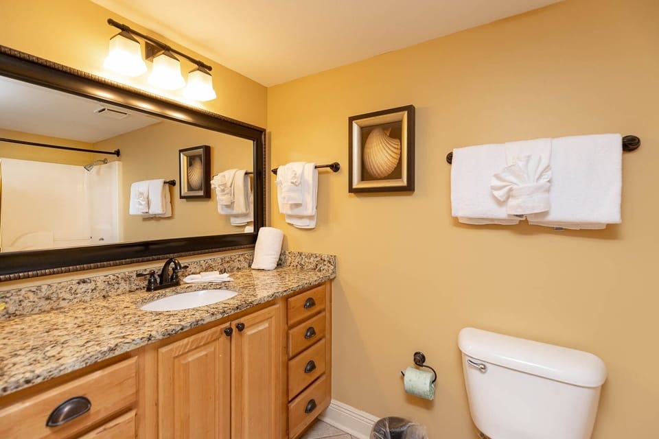 Warm yellow walls complement the granite countertop and elegant mirror in this guest bathroom with plush towels