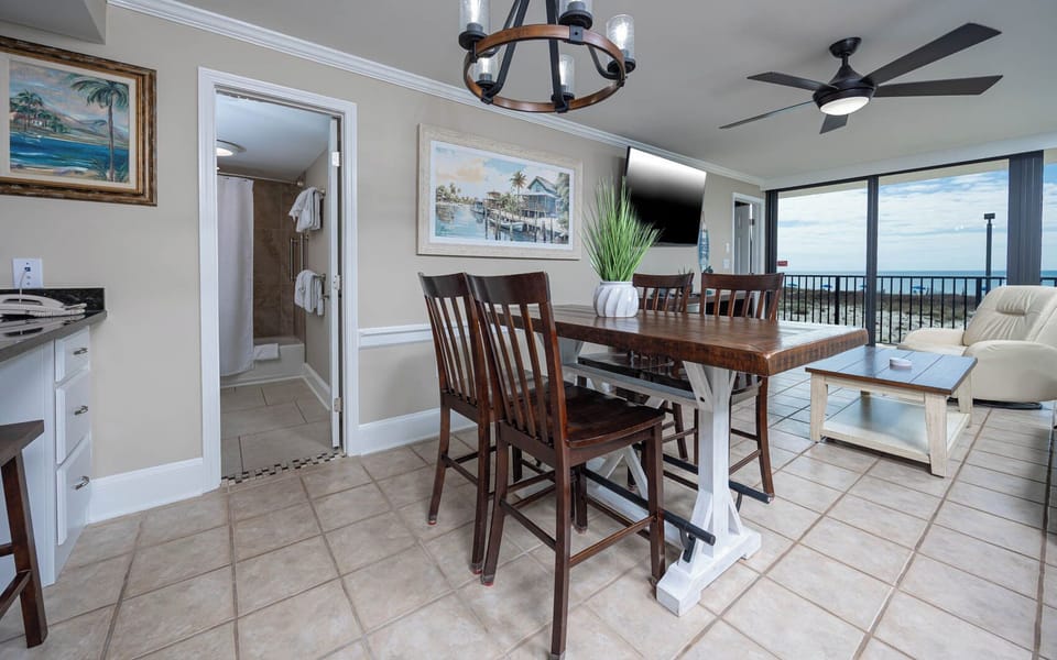 This dining area features a wooden table, comfortable seating, and a view of the beach through large windows