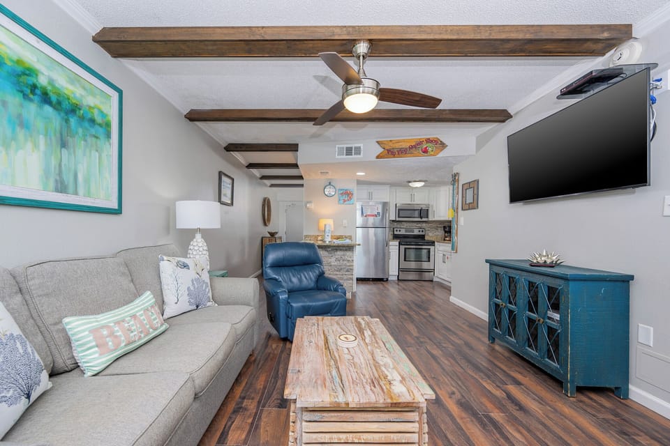 The living room features comfortable seating, a rustic coffee table, and a view leading to the kitchen area