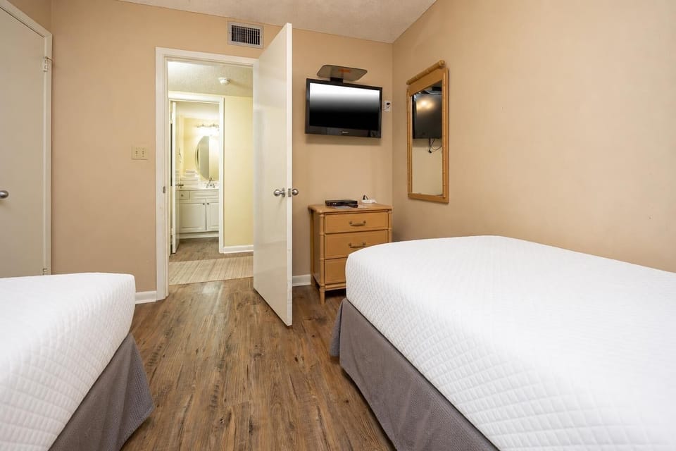 Cozy guest bedroom featuring two twin beds, a flat-screen TV, and an inviting view into the adjoining bathroom