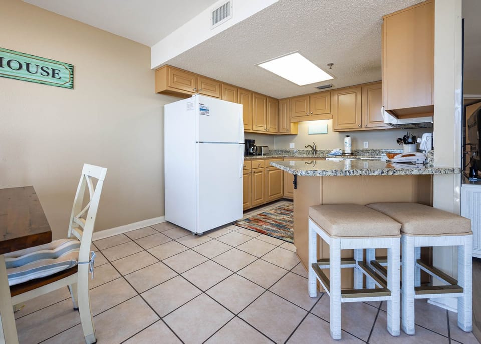 Bright kitchen area featuring granite countertops, a white refrigerator, and a breakfast bar with cushioned seating