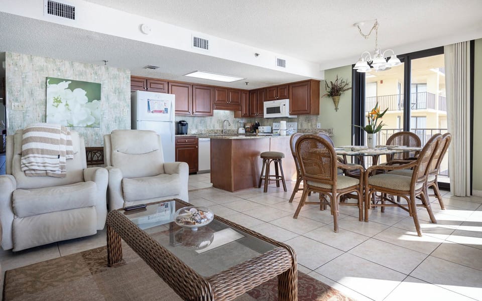 The open living area features two recliners, a glass coffee table, and a dining set surrounded by natural light
