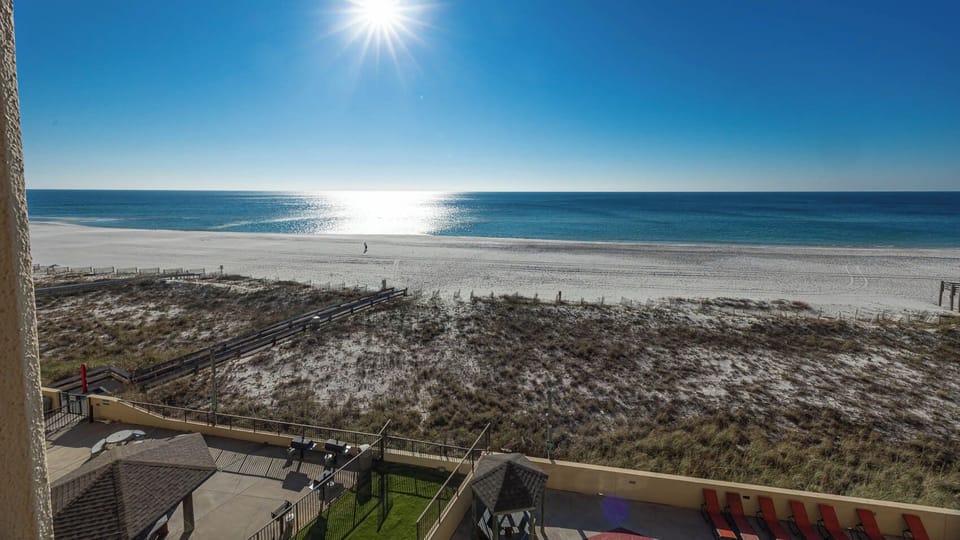 Serene beachfront view showcases glistening water and white sand, with a peaceful beach path visible in the foreground
