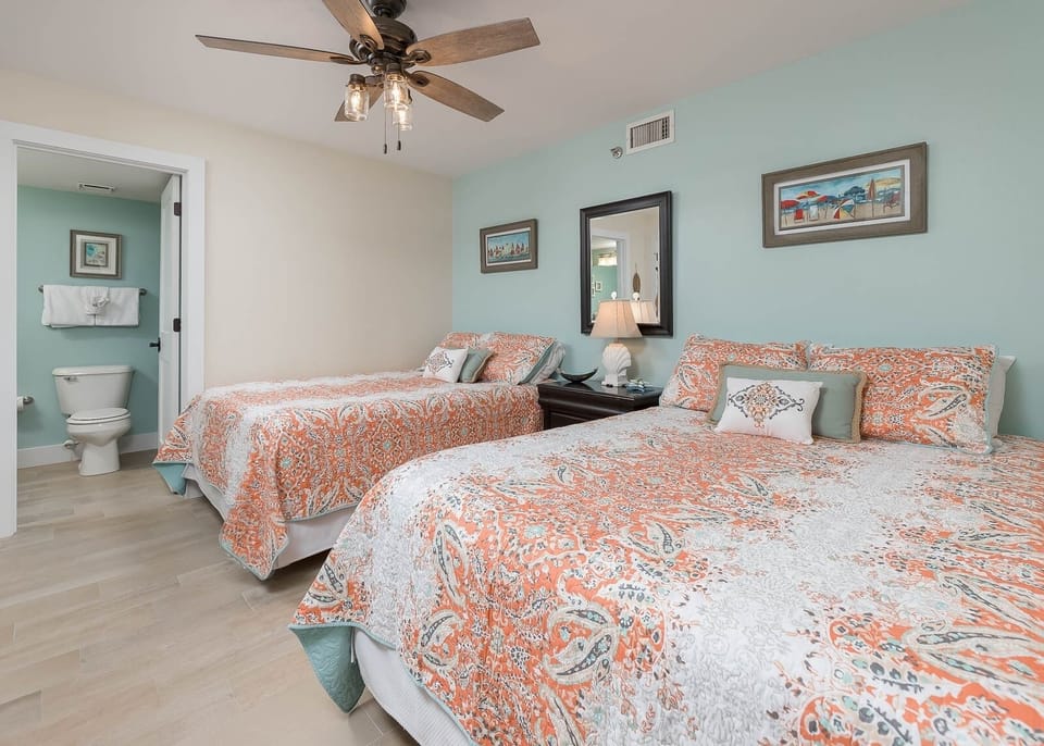 Two brightly colored queen beds in this inviting geust room, complemented by a ceiling fan and soft aqua walls