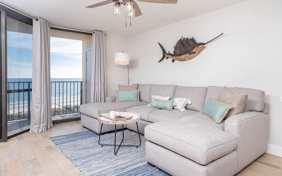 Living area features a large sectional sofa with colorful pillows, a stylish coffee table, and expansive gulf views