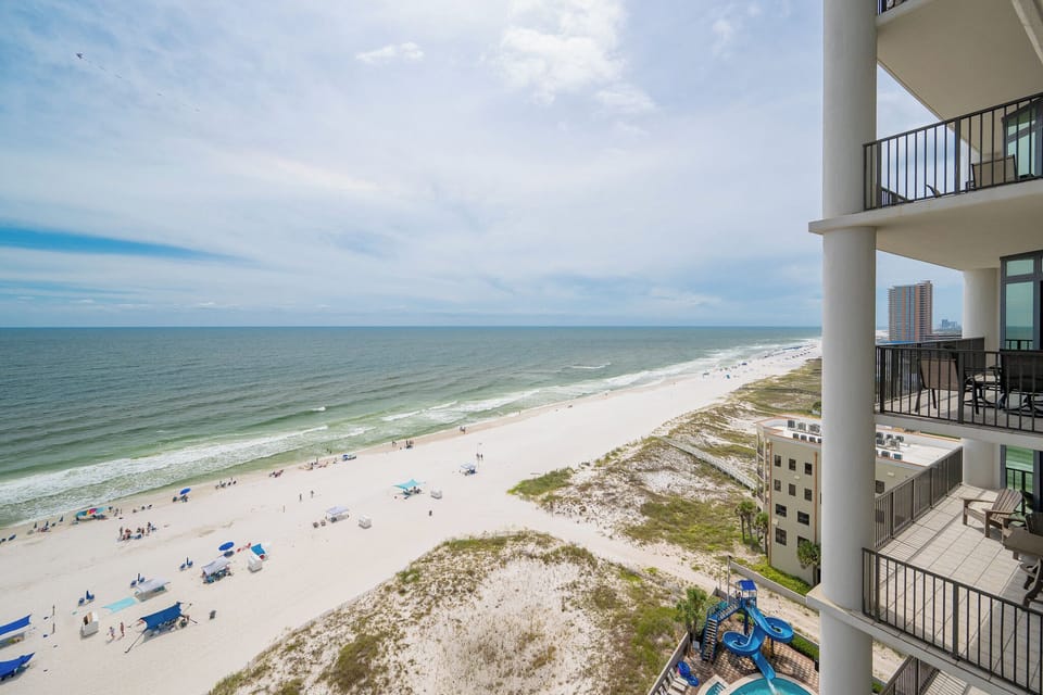 Breathtaking coastal view from the balcony, showcasing the sunny beach and umbrellas under a soft blue sky