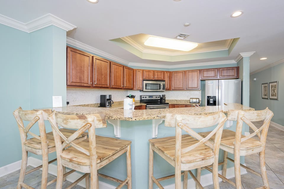 Luminous kitchen with granite countertops, stainless appliances, and stylish wooden bar stools for casual dining