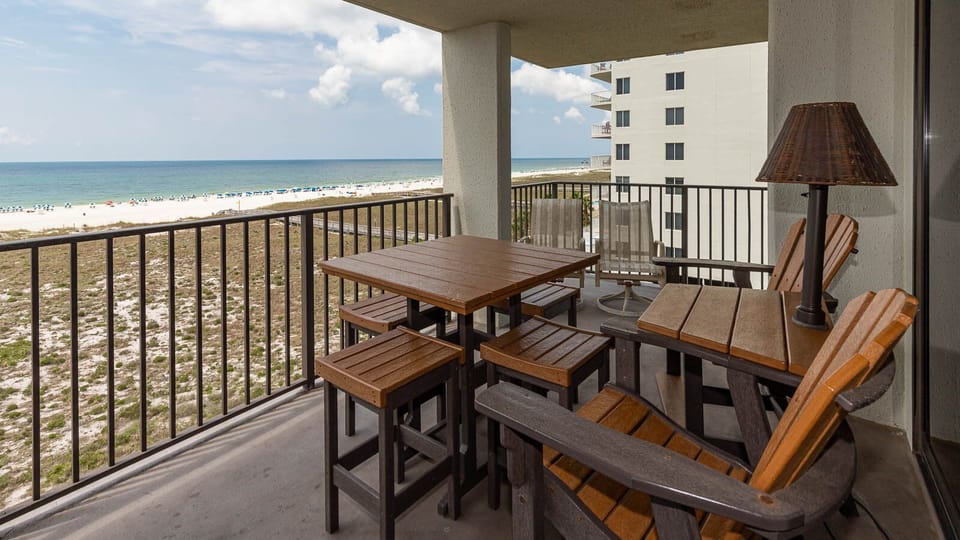 Balcony seating area features a wooden table and chairs, overlooking the beach with vibrant umbrellas dotting the shoreline