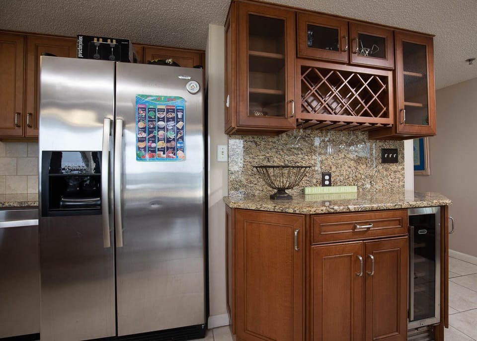 Sleek kitchen features a stainless refrigerator, granite countertops, and a wet bar with wine storage and glassware