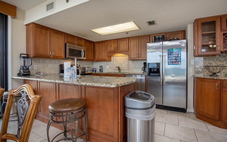 Warm wood cabinetry complements the granite countertops in this modern kitchen, featuring a breakfast bar with seating
