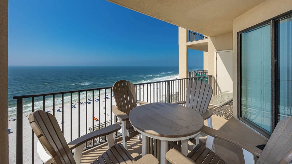 A private balcony features a round table and Adirondack chairs, offering a captivating view of the beach and sparkling water
