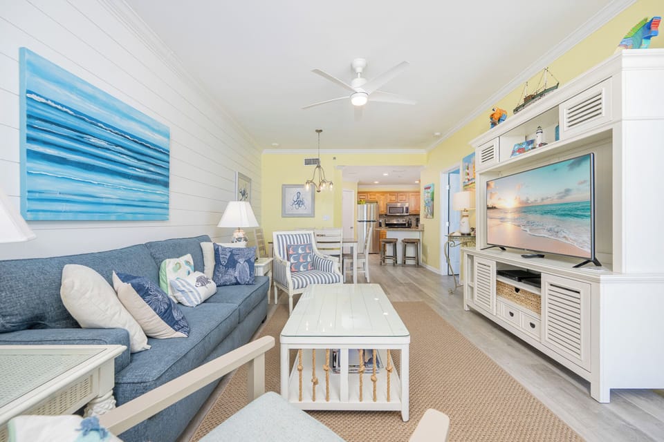 The living area features a blue sofa with decorative pillows and a queen sleeper, a light coffee table, and a large TV