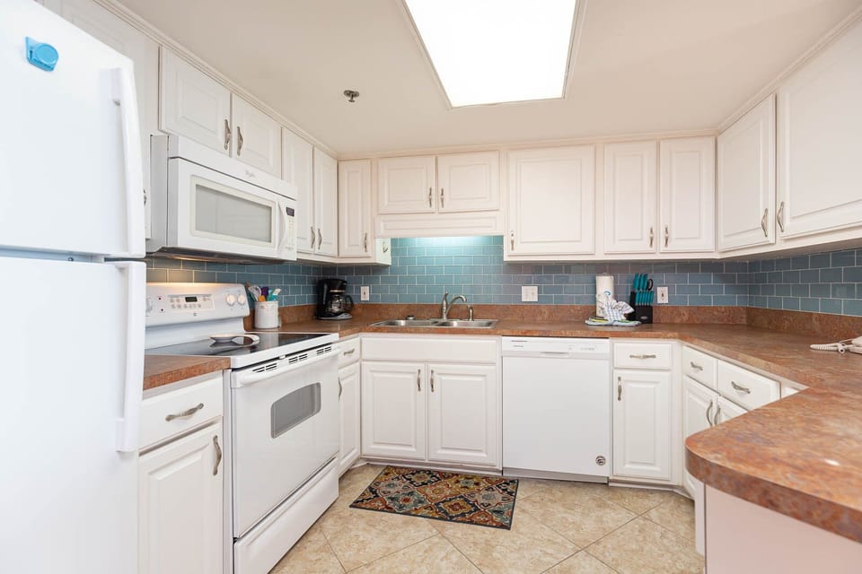 The kitchen features white cabinetry, a blue tiled backsplash, and a cozy rug, creating a welcoming cooking space