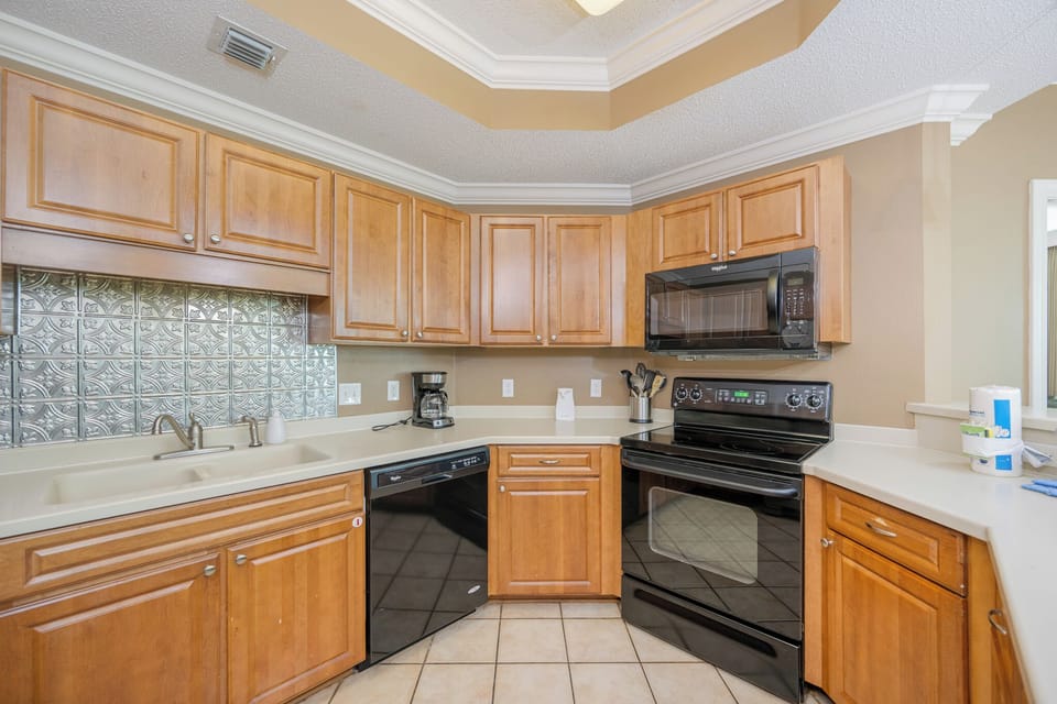 Prepare meals in this kitchen with wooden cabinetry, black appliances, and stylish backsplash