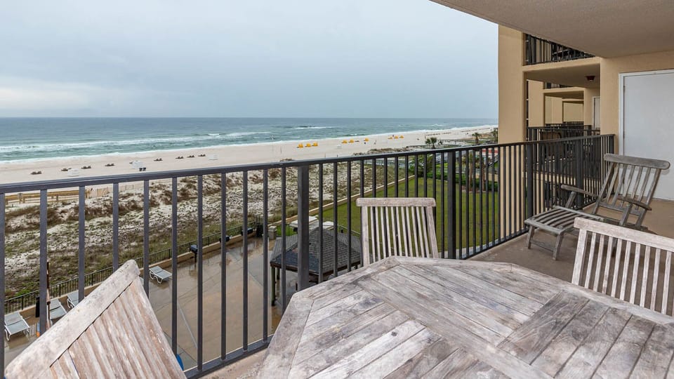 A spacious balcony features a wooden table and chairs, offering a serene view of the beach and gentle waves