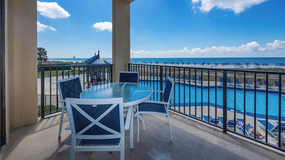 Enjoy a relaxing outdoor dining space with a glass table and chairs, overlooking the pool area and beach beyond