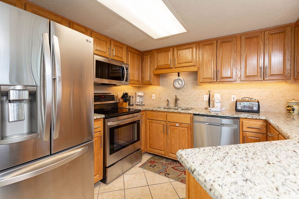 Wood cabinetry complements the granite countertops in this kitchen, featuring sleek stainless appliances and a coffee maker