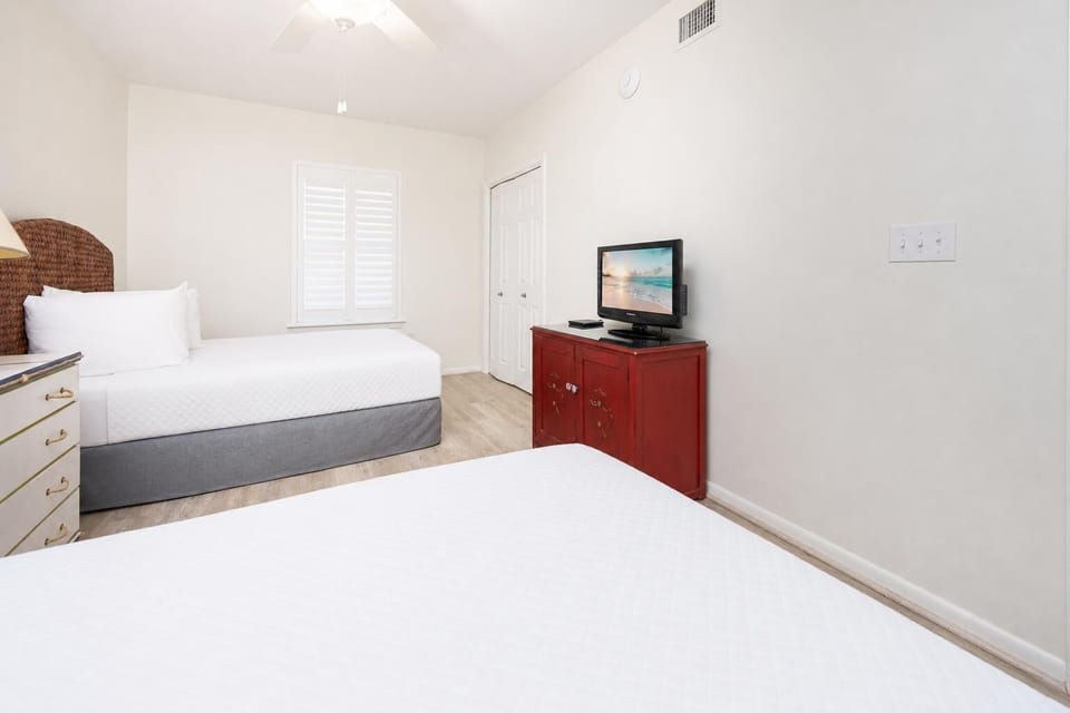 Relax in this comfortable guest bedroom featuring two double beds, a TV for entertainment, and natural lighting
