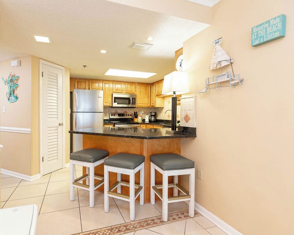 Modern kitchen area featuring wooden cabinetry, a breakfast bar with seating, and decorative beach accents