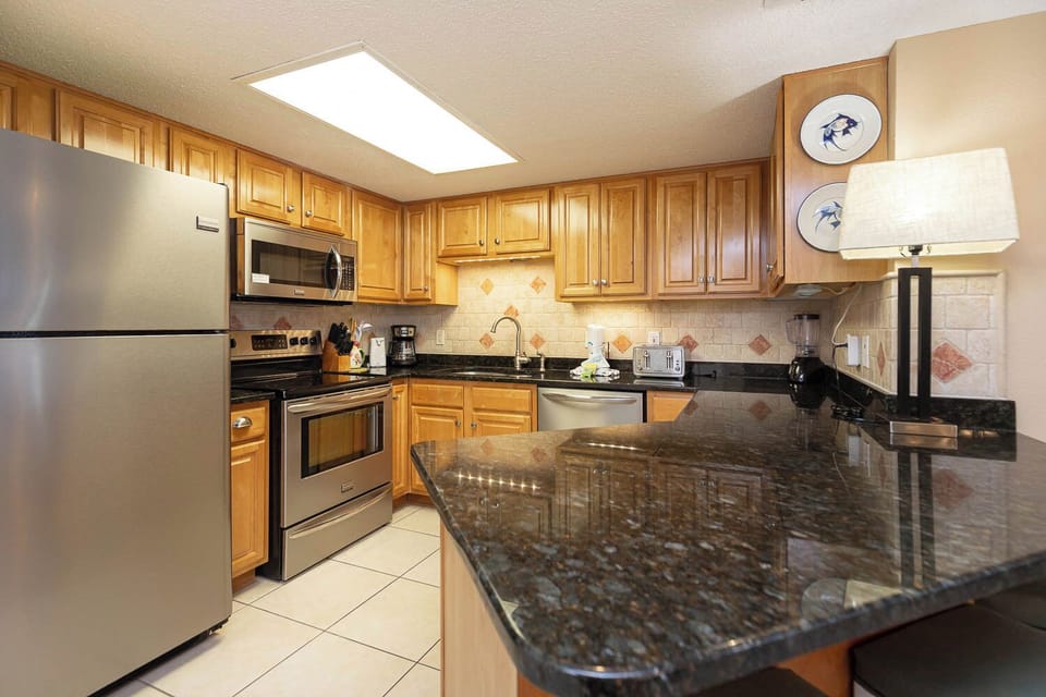 Kitchen features wood cabinetry, granite countertops, stainless appliances, and a breakfast bar with seating