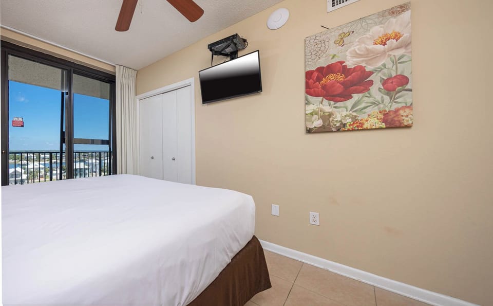 Cozy guest bedroom featuring a comfortable queen bed, a mounted TV, and a vibrant floral artwork