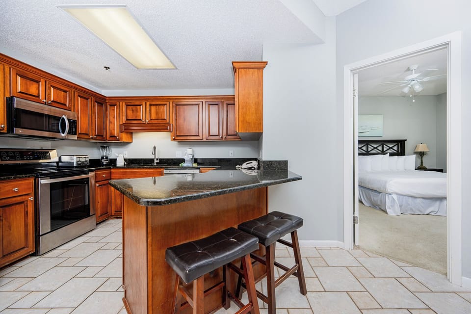 The kitchen features rich wooden cabinetry, a breakfast bar with seating, and a view into the cozy master suite