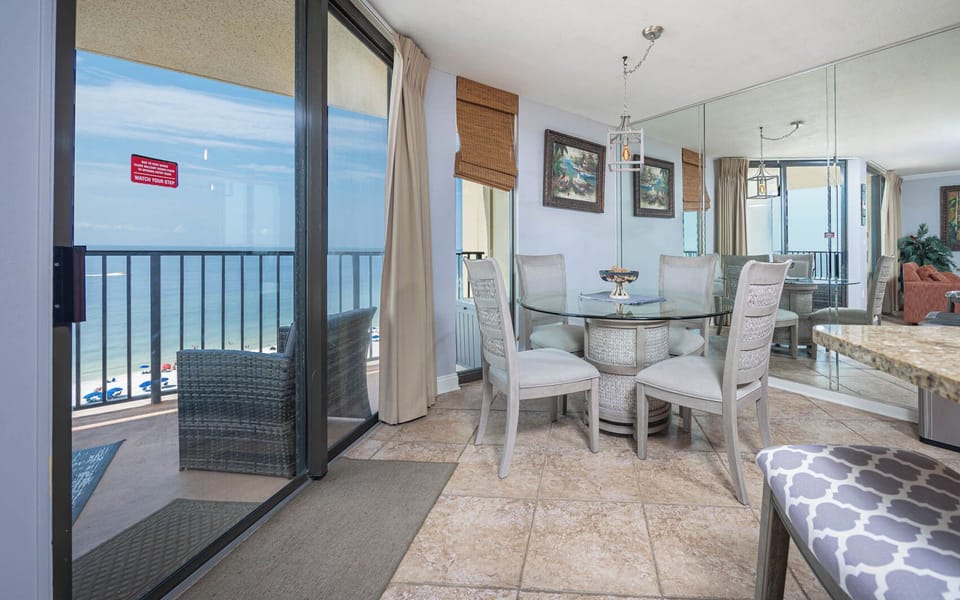 Bright dining area features a glass table surrounded by six chairs, with a view of the beach