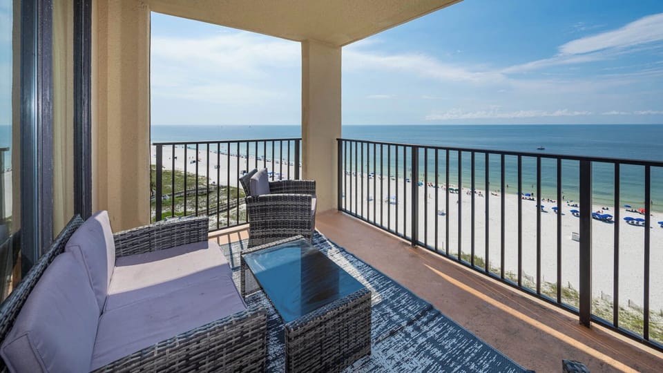 Relax on the balcony with stylish seating, overlooking the beach and vibrant umbrellas dotting the white sand below