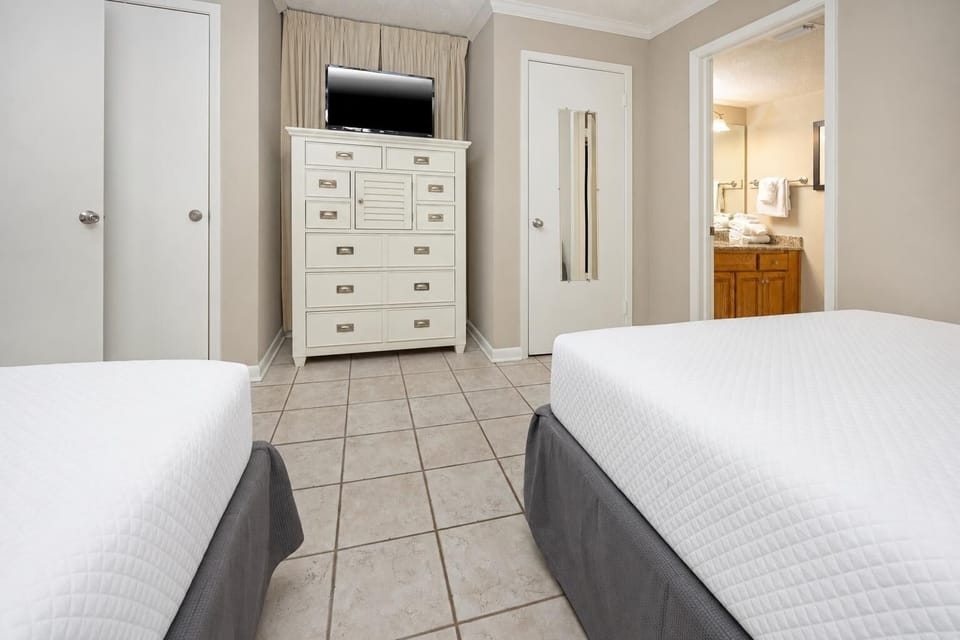 Relax in this cozy guest bedroom featuring two comfortable queen beds, a dresser, and adjoining bathroom