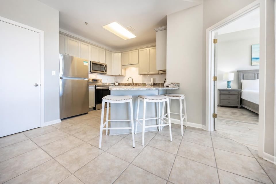 Kitchen area features a breakfast bar with white stools, granite countertops, and stainless appliances