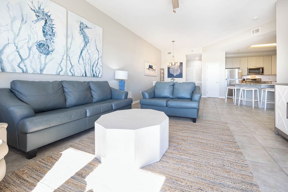 Light-filled living area features two blue leather sofas, a unique white coffee table, and a view into the modern kitchen