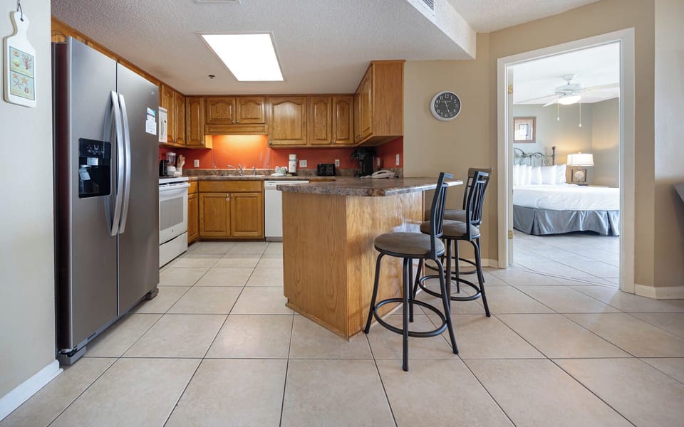 The kitchen features wooden cabinetry, a breakfast bar with seating, and a view into a the master suite