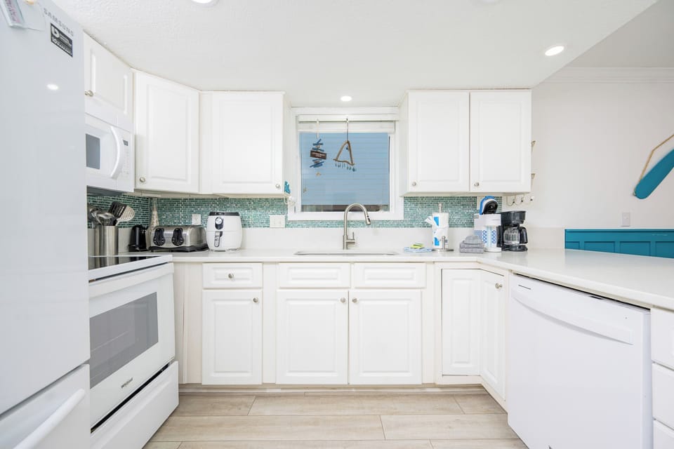 The kitchen features sleek white cabinetry, modern appliances, and a bright window view, perfect for meal prep and gatherings