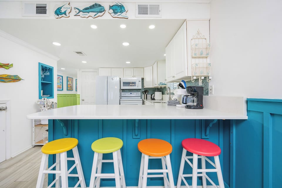 This vibrant kitchen features a bright blue bar area with colorful stools, light appliances, and a welcoming atmosphere